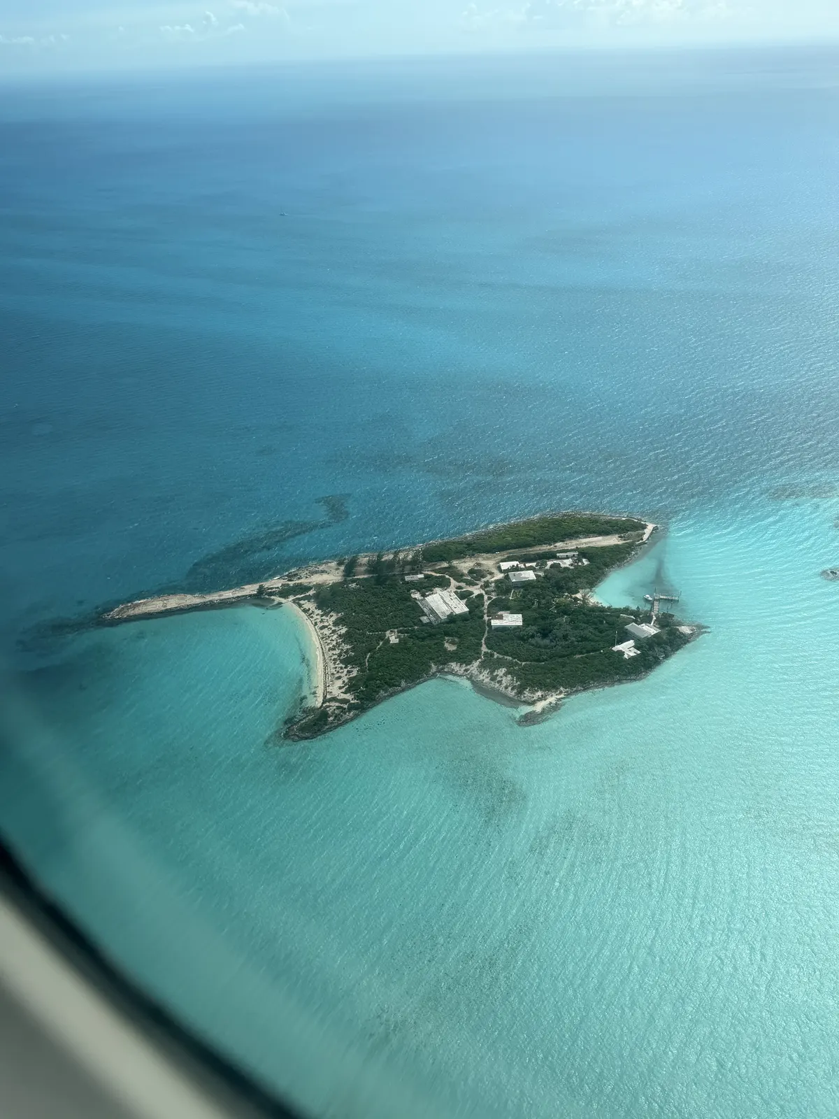 A small green cay ringed by turquoise shallows, seen from a plane window