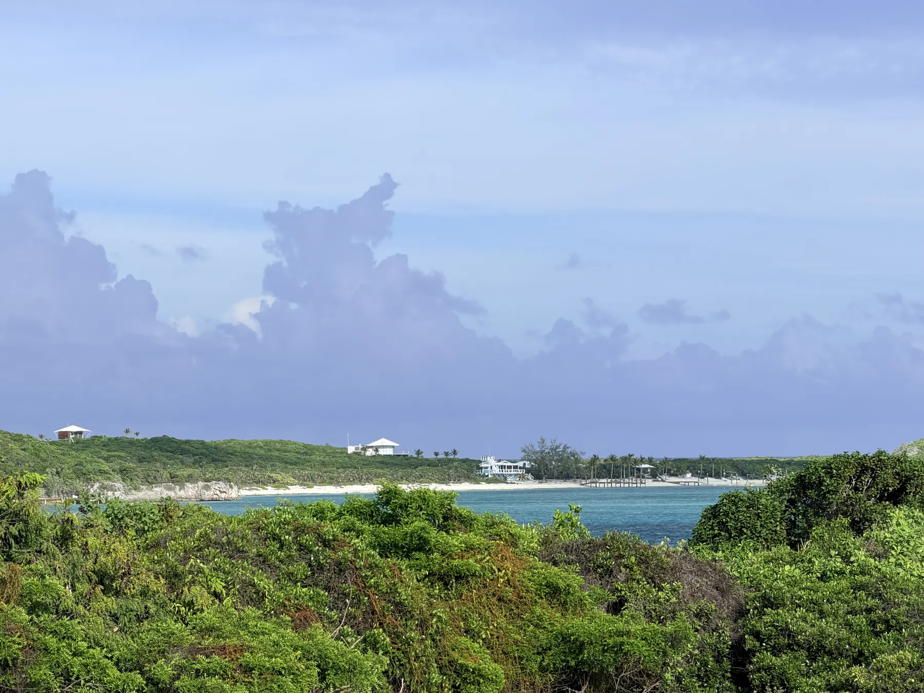 Green scrub sloping to blue water and a neighbouring cay under a wide sky
