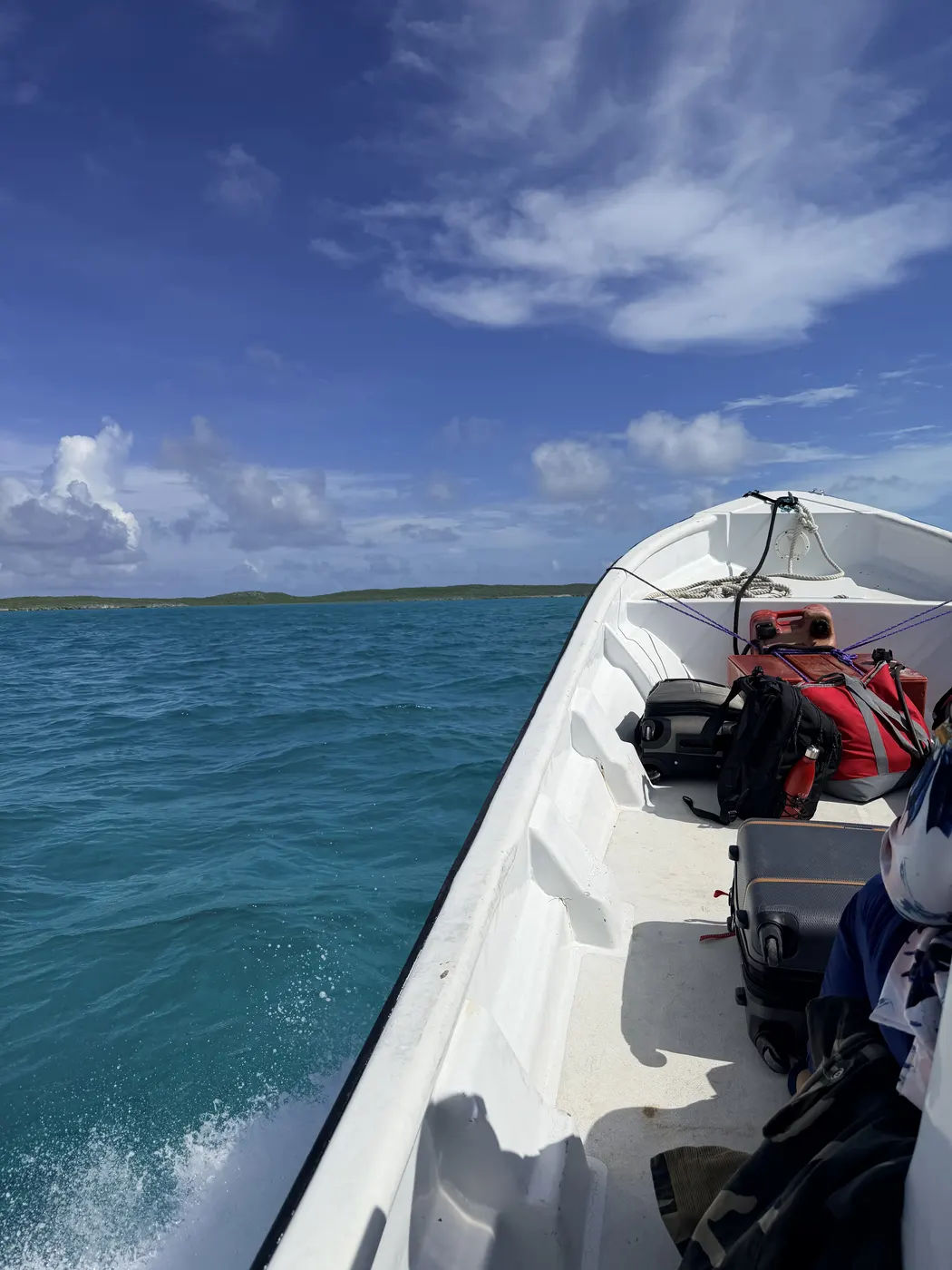 Bags and coolers in an open boat crossing turquoise water toward a low cay