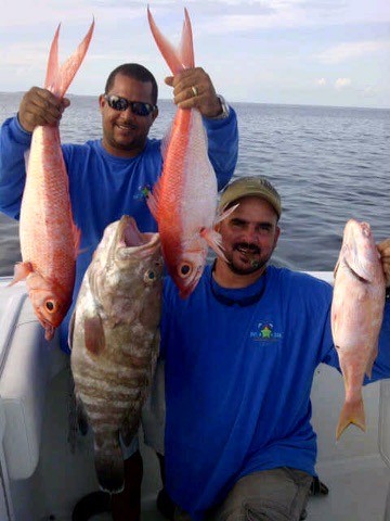 Two anglers displaying their catches aboard a boat